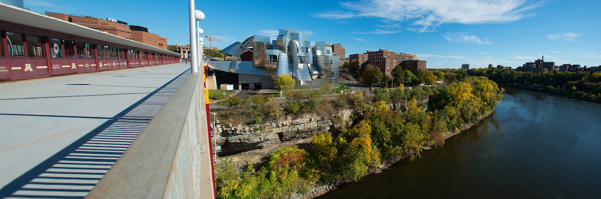 A summer view of the Weisman Museum and riverbank looking east from the Washington Ave Bridge.